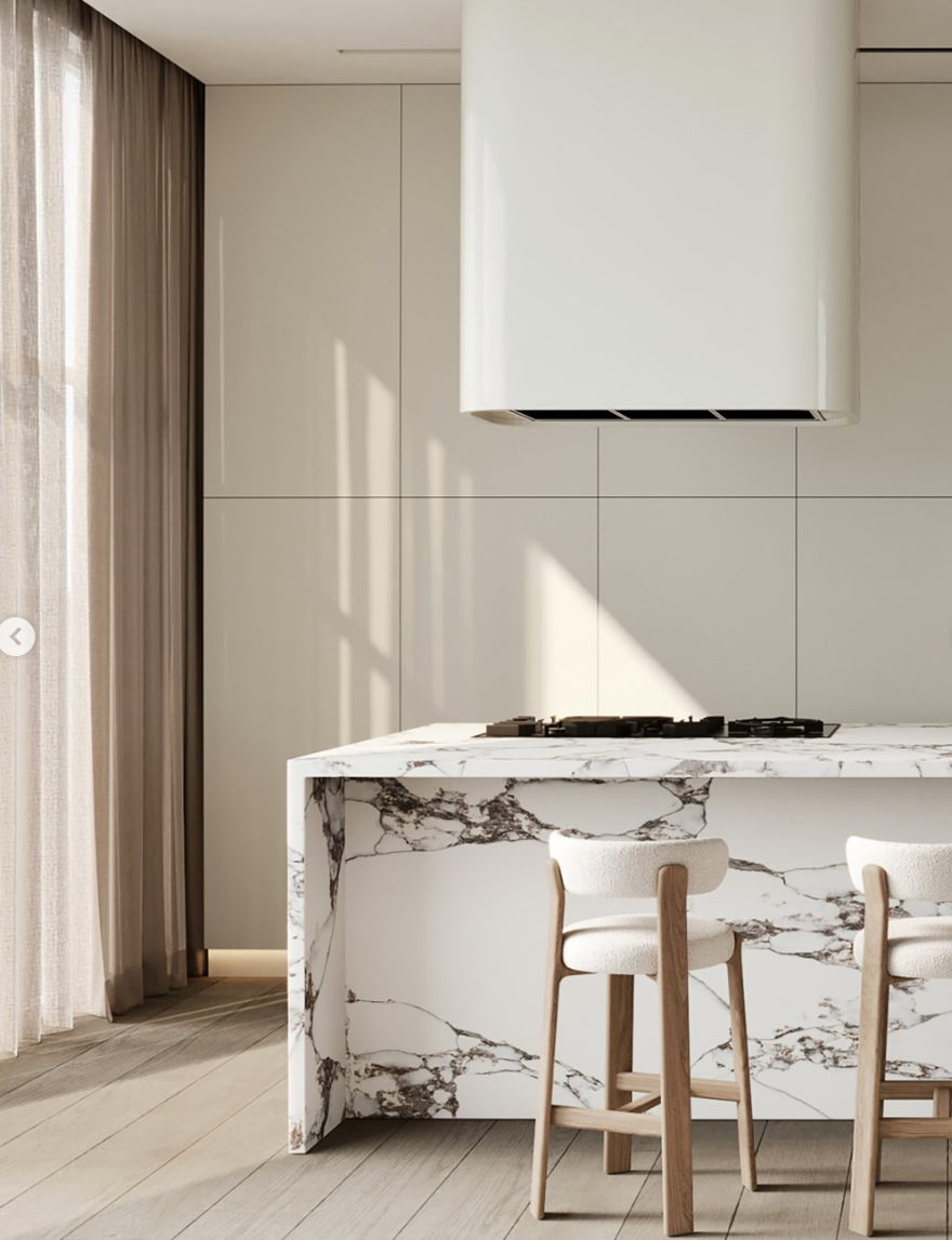 The image shows a modern kitchen with white countertops, marble backsplashes, and a sleek stainless steel range hood, complemented by minimalist, white-washed cabinetry and cascading sheer curtains.